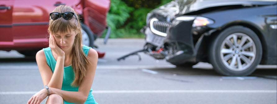women kneeling on side of road after a car accident