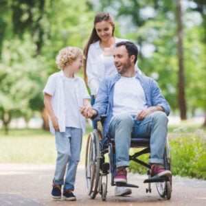 mother rolling wheelchair with disabled father in park with their son